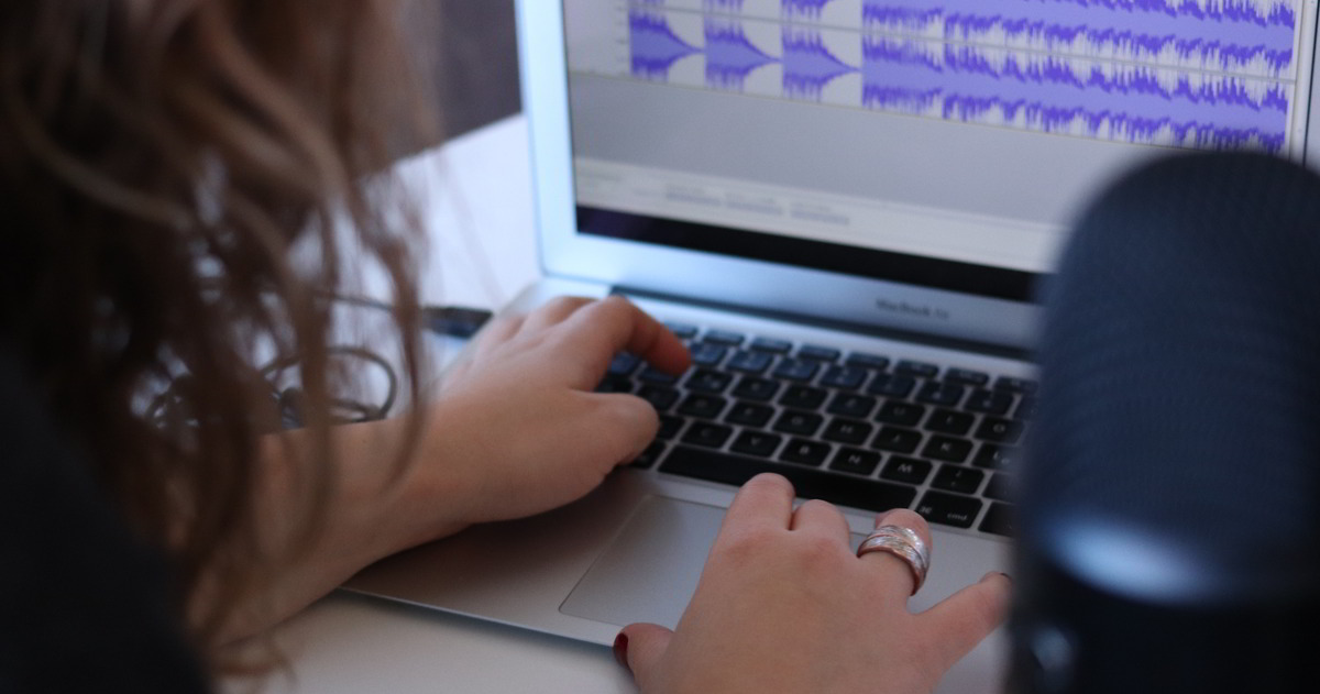 Schulterblick: Frau sitzt an Laptop und bearbeitet Audiofiles