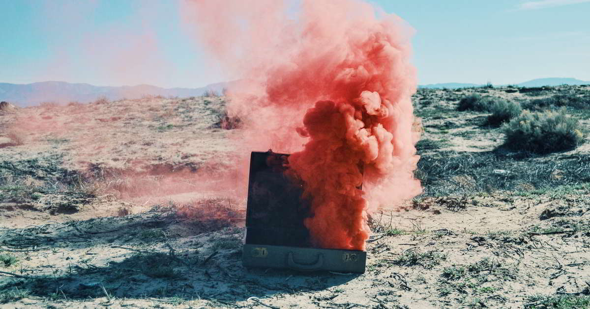 Roter Qualm aus Koffer In einer Wüstenlandschaft steht ein Koffer aus dem roter Qualm hochsteigt