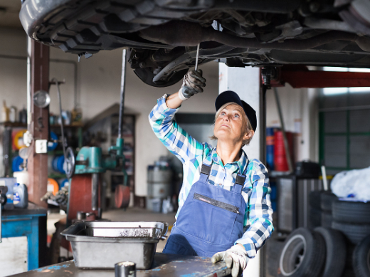 Andere Bildsprache: Eine ältere Automechanikerin schraubt an einem Auto in einer Werkstatt